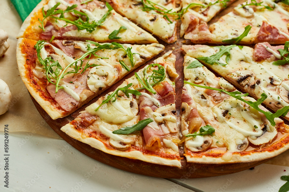 Sliced Freshly baked pizza with ham, rukkola and mushrooms served on wooden background with tomatoes, sauces and herbs. Food delivery concept. Restaurant menu Sliced Freshly baked pizza with ham, rukkola and mushrooms served on wooden background with tomatoes, sauces and herbs. Food delivery concept. Restaurant menu