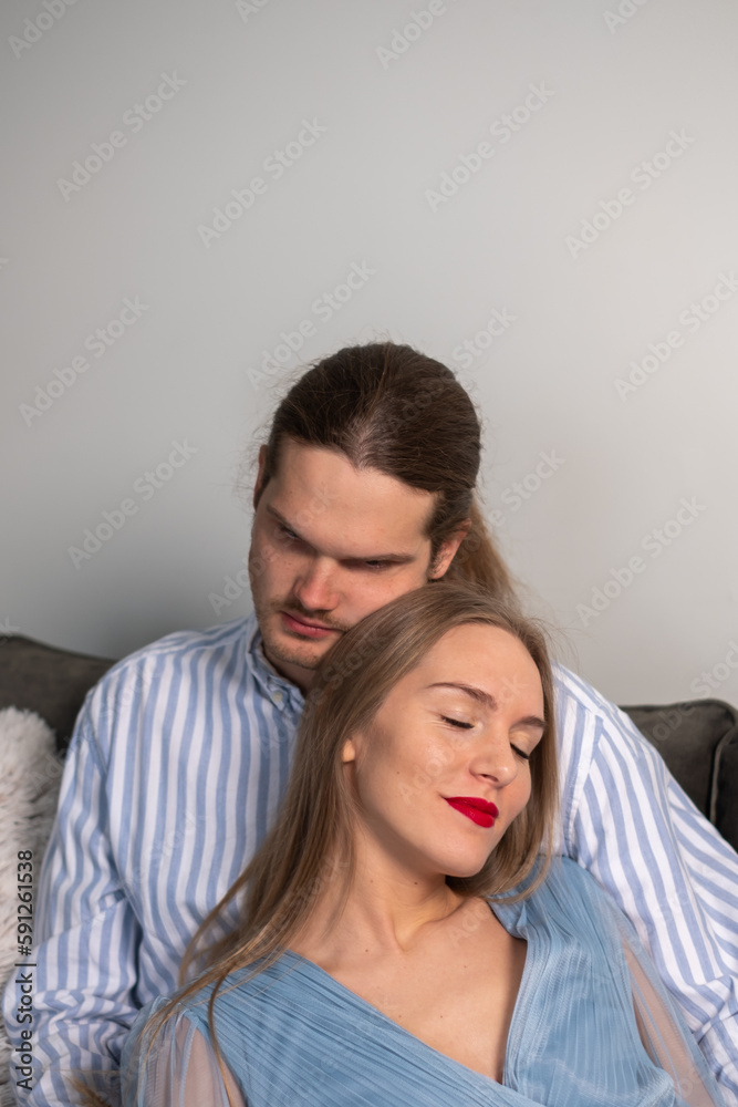 Fototapeta premium Happy man in striped shirt hugs beautiful loving woman with long hair, red lips, light blue dress. A couple enjoying a romantic time together.