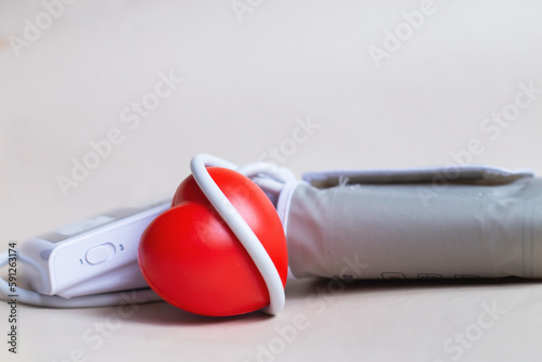 Red heart and white electronic tonometer isolated on beige background