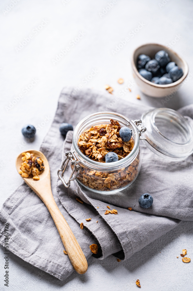 Fototapeta premium Homemade baked granola with nuts and fresh blueberry in a jar on a light background with napkin. Healthy vegetarian muesli for breakfast.