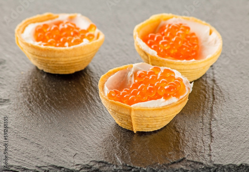 Tartlets filled with red salmon caviar on a black stone background