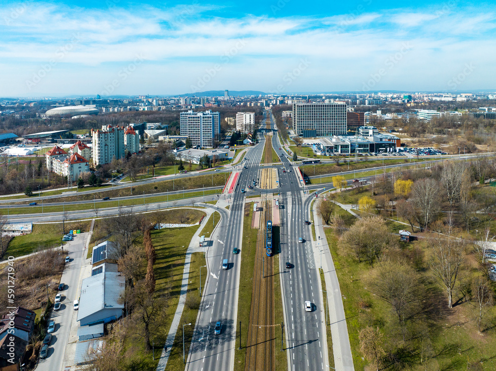 Fototapeta premium City highway multilevel crossroad in Krakow, Poland. Tramway and tram near a tram stop, cars, zebra crossings, cycle tracks and public park. Aerial view