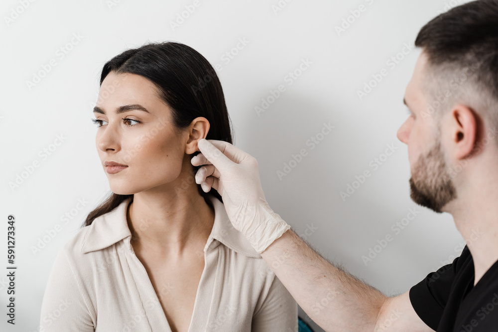 Otoplasty is surgical reshaping of the pinna, or outer ear for correcting an irregularity and improving appearance. Surgeon doctor examines girl ear before otoplasty cosmetic surgery. Otoplasty is surgical reshaping of the pinna, or outer ear for correcting an irregularity and improving appearance. Surgeon doctor examines girl ear before otoplasty cosmetic surgery.