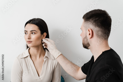 Otoplasty is surgical reshaping of the pinna, or outer ear for correcting an irregularity and improving appearance. Surgeon doctor examines girl ear before otoplasty cosmetic surgery.