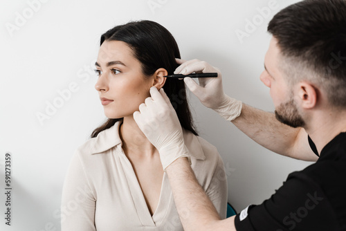 Otoplasty markup for surgical reshaping of the pinna, or outer ear for correcting an irregularity and improving appearance. Surgeon doctor marking girl ear before otoplasty cosmetic surgery. photo