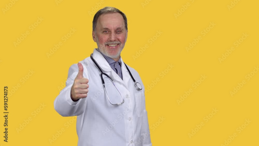 Smiling male senior doctor wearing stethoscope giving his thumb up. Isolated on orange. Smiling male senior doctor wearing stethoscope giving his thumb up. Isolated on orange.