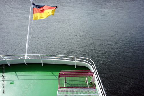 Im Wind wehende deutsche Fahne in Schwarz, Rot und Gold bei Sonnenschein am Heck eines Ausflugsschiff auf dem Edersee bei Waldeck im Landkreis Waldeck-Frankenberg in Hessen photo