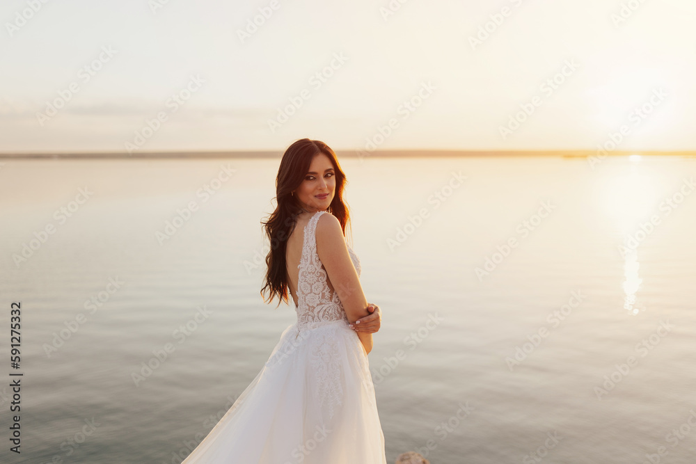 Beautiful stylish young bride is posing at the sea view. Wedding ceremony outdoors on the seashore. Summer sunset. Beautiful stylish young bride is posing at the sea view. Wedding ceremony outdoors on the seashore. Summer sunset.