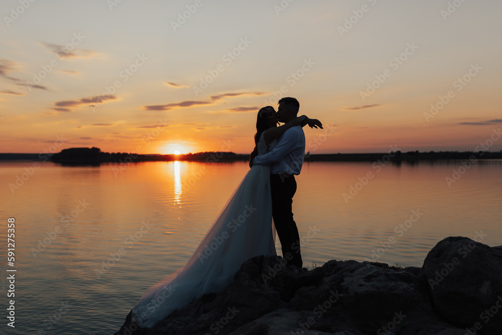 Silhouette of newlyweds bride and groom are hugging and kissing on sunset  on beach. Loving couple by the sea. Sea romantic ceremony. 