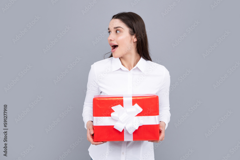 Attractive woman with present box posing with surprised face expression on gray background. Girl holding gift decorated with ribbon. Valentine day, birthday, happy new year gift people concept. Attractive woman with present box posing with surprised face expression on gray background. Girl holding gift decorated with ribbon. Valentine day, birthday, happy new year gift people concept.