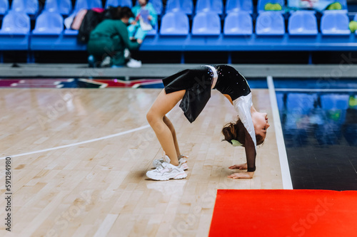 Beautiful girl, child, sportswoman cheerleader in uniform dancing, showing the bridge, showing the elements of gymnastics in the gym at the competition. The concept of sports, cheerleading.