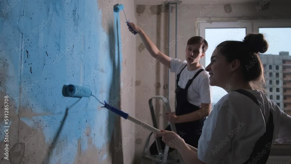 Couple in new home during repair works painting wall together. Happy family holding paint roller
