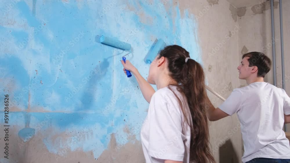 Couple in new home during repair works painting wall together. Happy family holding paint roller