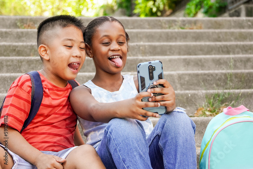 Happy multiethnic children taking selfie stiking out the tongue. Use of technologies and social media by children photo