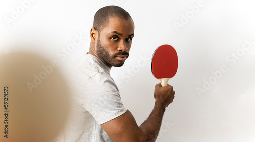 An adult dark-skinned man posing against a white background with a ping pong racket waiting to receive the ball. Ping pong player concept. photo