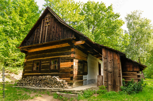 Beautiful wooden old house in green forest with pile of wood stored in front, ready for winter.