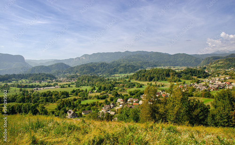 A view of green pastures, a nice village and the Julian Alps in Slovenia. Beautiful day for hiking.
