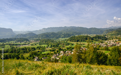 A view of green pastures, a nice village and the Julian Alps in Slovenia. Beautiful day for hiking.