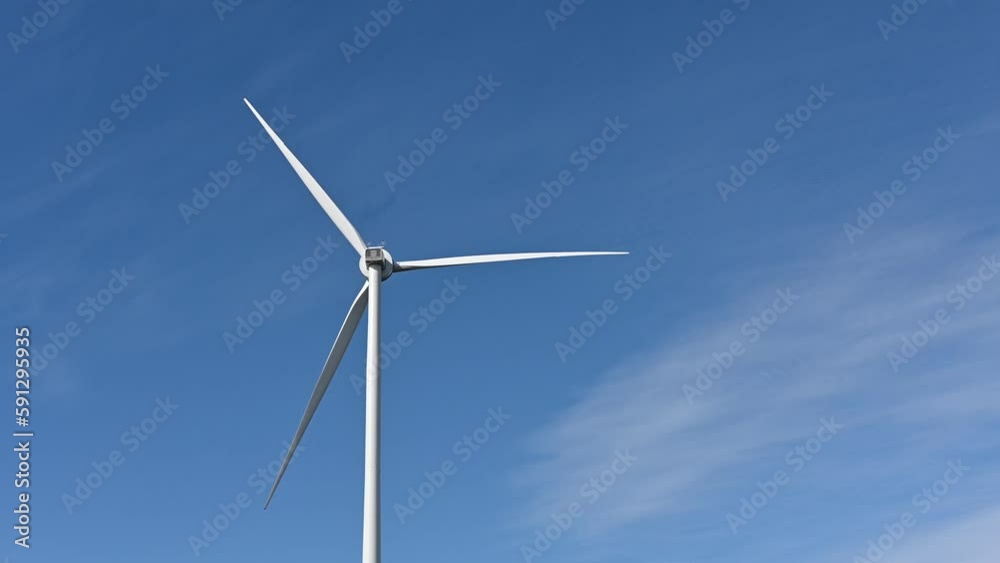 A large wind turbine rotates but gradually slows to a stop. Blue sky with wispy clouds behind. A large wind turbine rotates but gradually slows to a stop. Blue sky with wispy clouds behind.