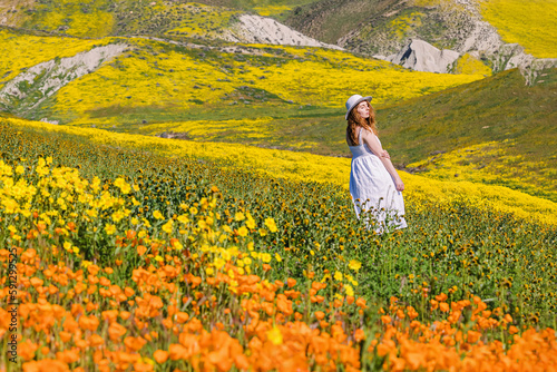 Woman in a white dress enjoying sunny weather among beautiful meadow full of wildflowers.