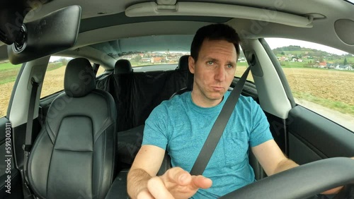 DASHCAM: Singing and dancing young man at driving a car through countryside. Male person in blue shirt listening to the music and having fun while commuting. A bit distracted guy behind steering wheel photo