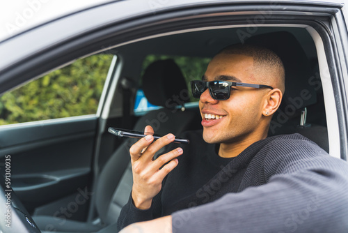 Smiling African American man sitting in a driver seat and talking on a speakerphone . High quality photo