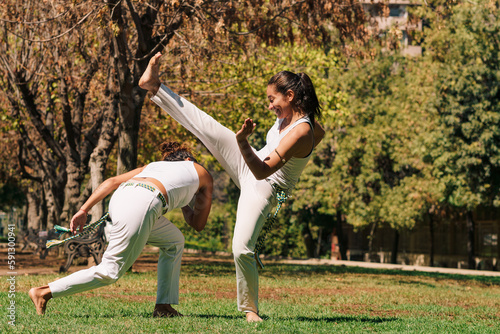 mujeres practicando patadas, ejercicios y capoeira en la ciudad con su ropa de capoeira en un parque verde en un día soleado.