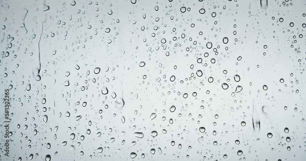 Raindrops on the window dripping down in autumn monsoon. Rainy weather drops knock on window glass. Gray natural background.