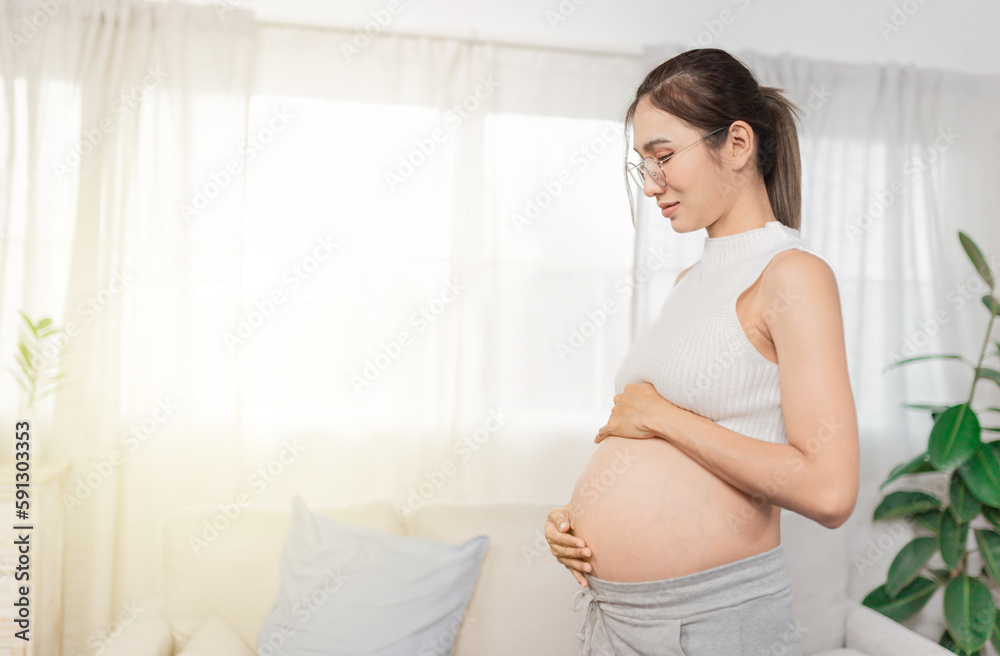 pregnant Asian people stand in white room, she use her hand touch on her abdomen, she feeling love and care her daughter, pregnancy health care promotion pregnant Asian people stand in white room, she use her hand touch on her abdomen, she feeling love and care her daughter, pregnancy health care promotion