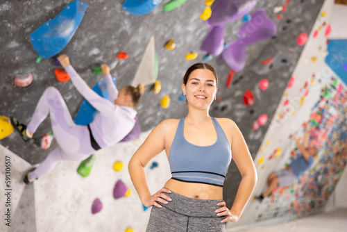 Smiling sporty young girl posing near climbing wall at bouldering gym after workout  feeling accomplished and energized