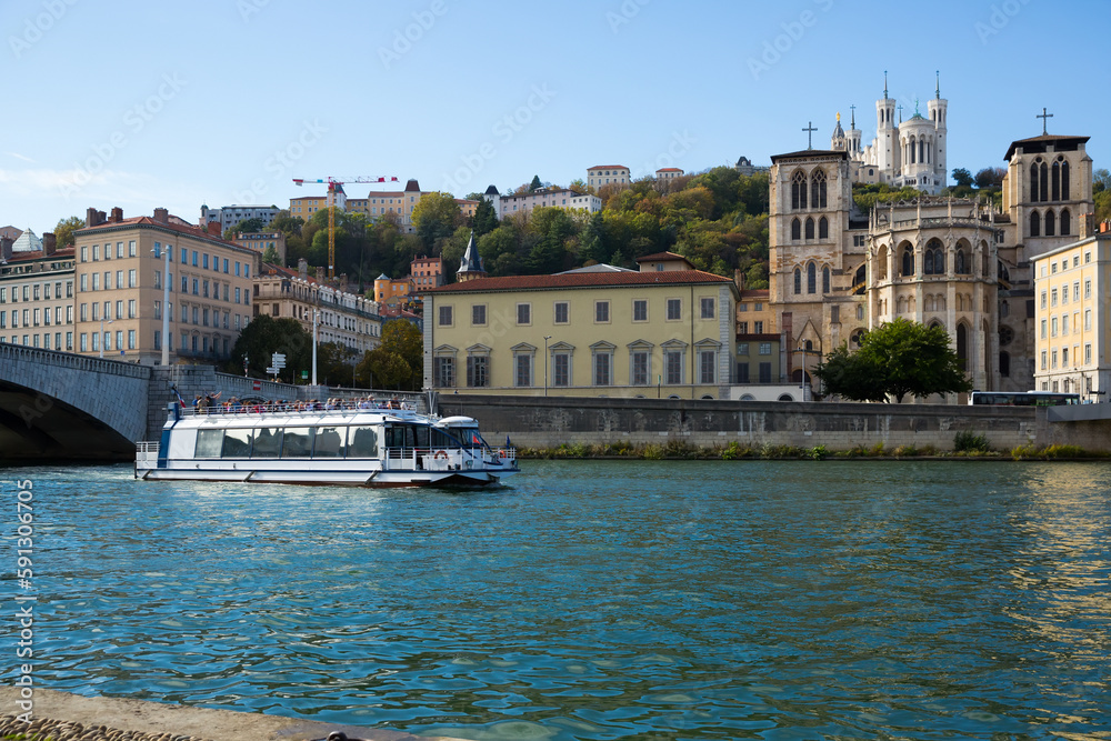 Modern pleasure ship sailing on Saone river along Fourviere hill in Lyon on sunny autumn day, France..