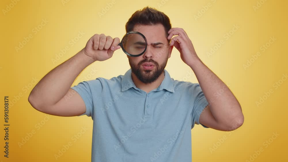 Investigator researcher scientist man holding magnifying glass near face looking into camera with big zoomed funny eyes, searching analysing. Excited caucasian guy isolated on yellow studio background Investigator researcher scientist man holding magnifying glass near face looking into camera with big zoomed funny eyes, searching analysing. Excited caucasian guy isolated on yellow studio background