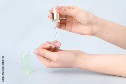 Woman applying oil onto cuticles on light background