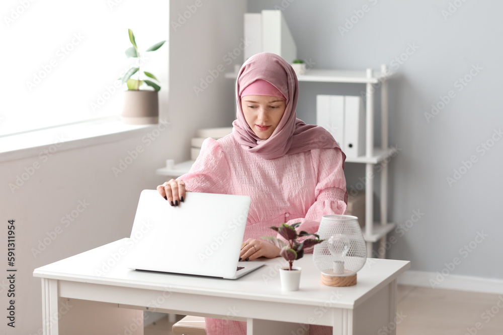 Muslim female programmer working with laptop at table in office Muslim female programmer working with laptop at table in office