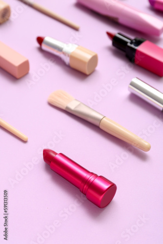 Decorative cosmetics with makeup brushes on lilac background