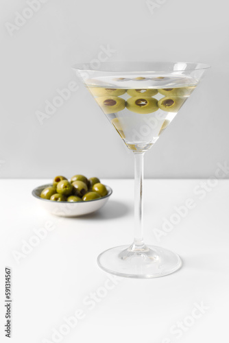 Glass of martini and olives on light background