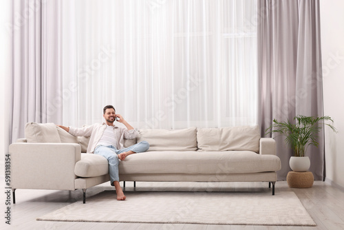 Man talking smartphone near window with beautiful curtains in living room
