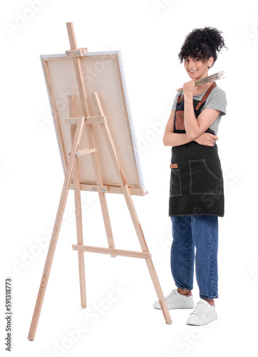 Young woman holding brush near easel with canvas against white background