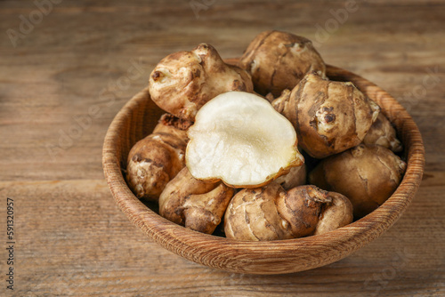 Bowl with whole and cut Jerusalem artichokes on wooden table, closeup