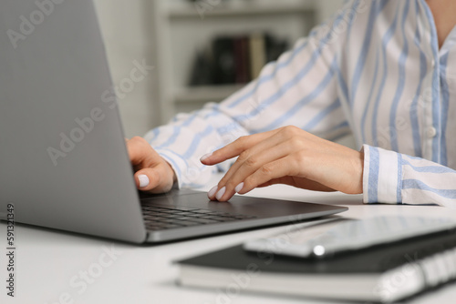Woman working with laptop at white desk indoors, closeup