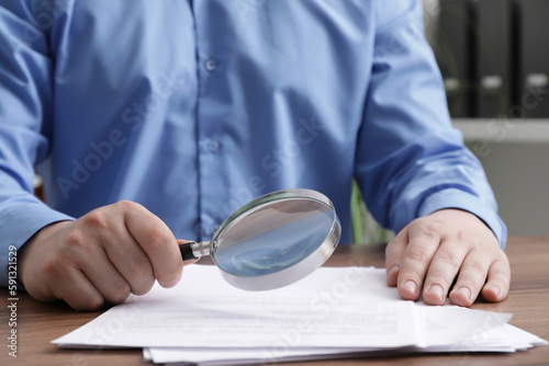 Man looking at document through magnifier at wooden table, closeup. Searching concept