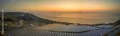 Panoramic view of solar panels and turbines on coastal energy farm at sunset