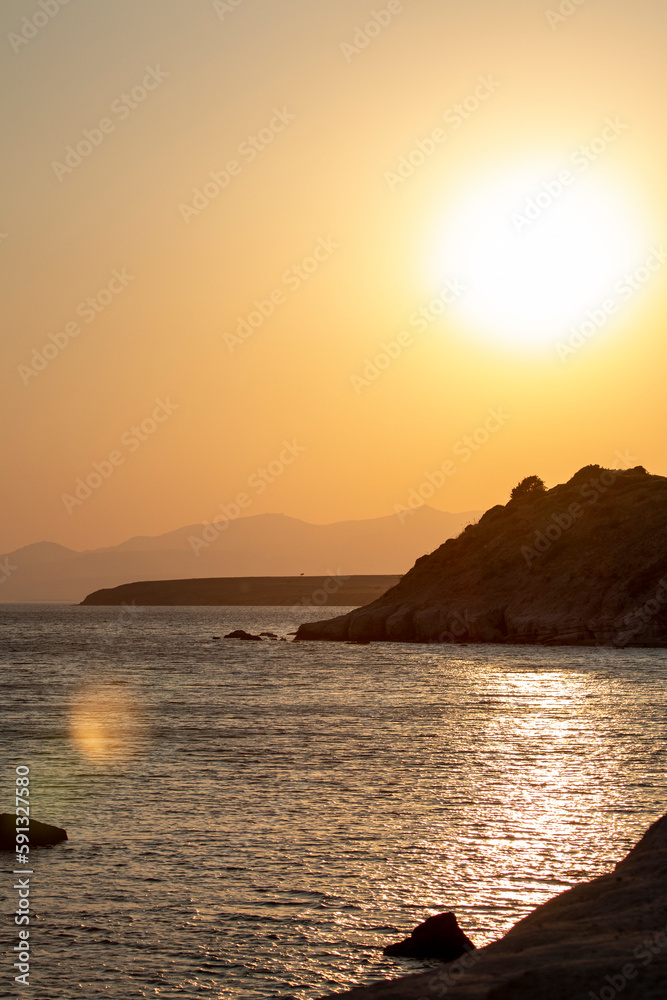 Sunset over the sea with rocks and mountains in the background. Sunset on the coast. Sunlight reflecting off the sea.
