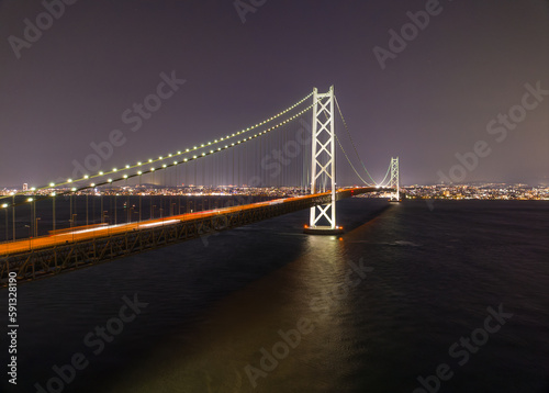 Car lights blur over Akashi Bridge with distant city at night