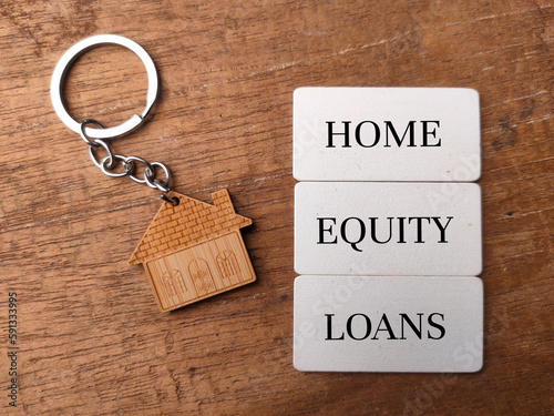 Wooden house keychain with text HOME EQUITY LOANS on wooden background.