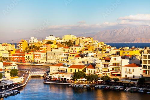 Greece. Crete island. Top view of Agios Nikolaos resort mediterranean town and Voulismeni lake promenade in sunset light. Scenic cityscape. Summer travel and seaside recreation concept