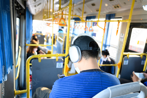 A man wearing cap on the passenger seat of the bus listens to music.Traveler sitting outside the window public transportation.Tourist is traveling and looking through the bus window.