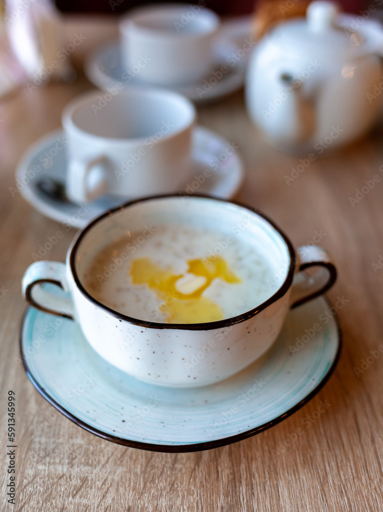 A beautiful white plate with oatmeal porridge and butter on the table. Perfect breakfast in the city cafe with oatmeal, coffee and tea on the round wooden table.