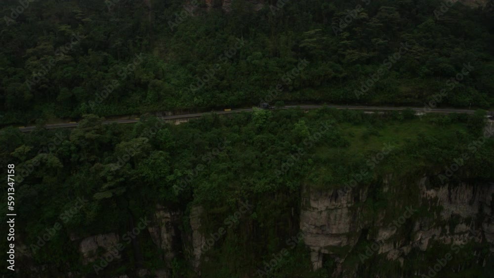 Aerial side view follow of black truck passing luxury cliff side home in jungle Aerial side view follow of black truck passing luxury cliff side home in jungle