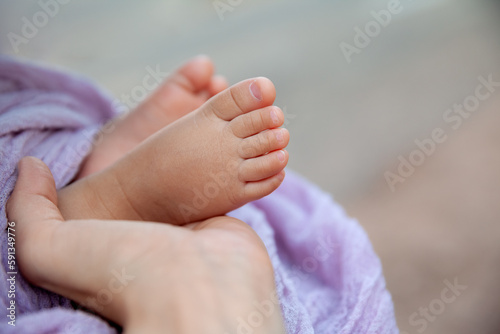 Newborn baby feet in mother's hand at natural light, tiny toes of infant girl